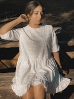 A serene moment of a woman seated on a wooden bench, wearing a soft linen dress and light scarf.