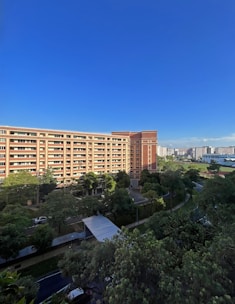A modern red-brick residential building surrounded by green trees under a clear sky.