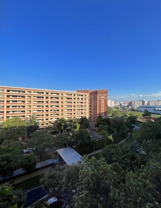 A modern red-brick residential building surrounded by green trees under a clear sky.