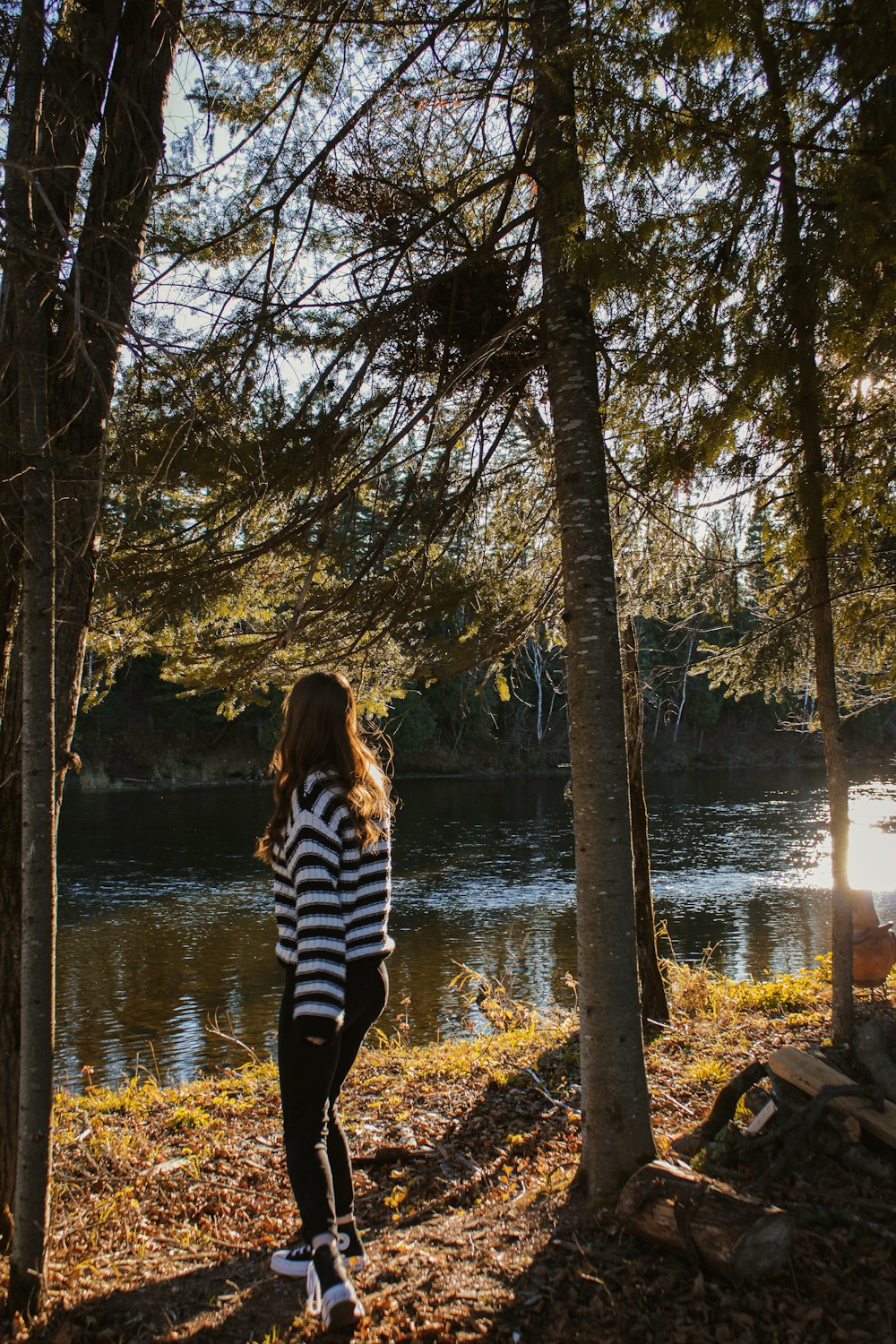 a girl standing in the woods looking at a lake