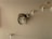 A brown tabby cat is perched on a small wall-mounted platform, which is one of several arranged vertically on a plain wall. The cat appears relaxed and is staring directly at the camera. Above the cat are more platforms, with another cat lying on the top platform.