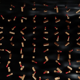 Numerous red lipsticks with ornate gold cases are scattered across a dark, black background, creating a visually striking pattern.