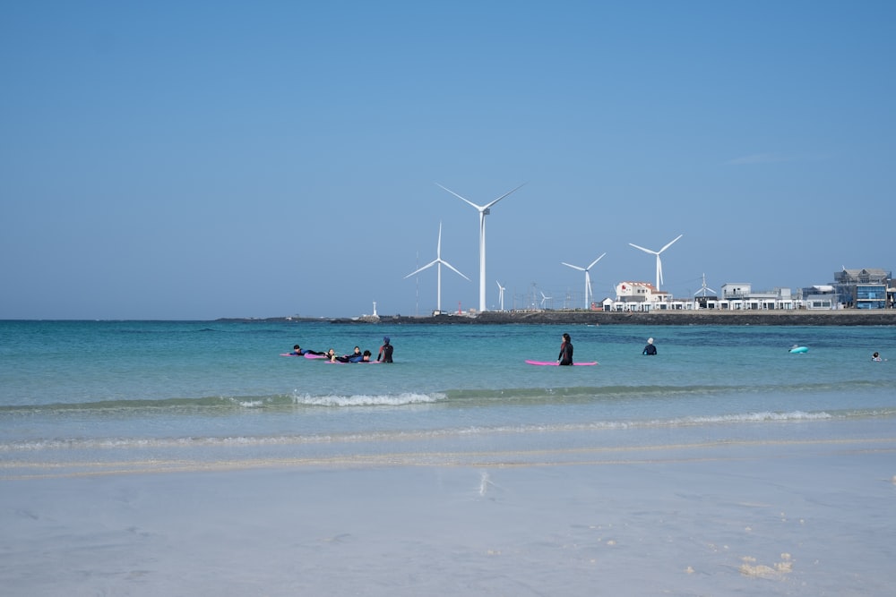 a group of people in the ocean with wind turbines in the background