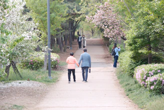 A serene shot of the couple walking hand in hand along a path lined with lilac blossoms.