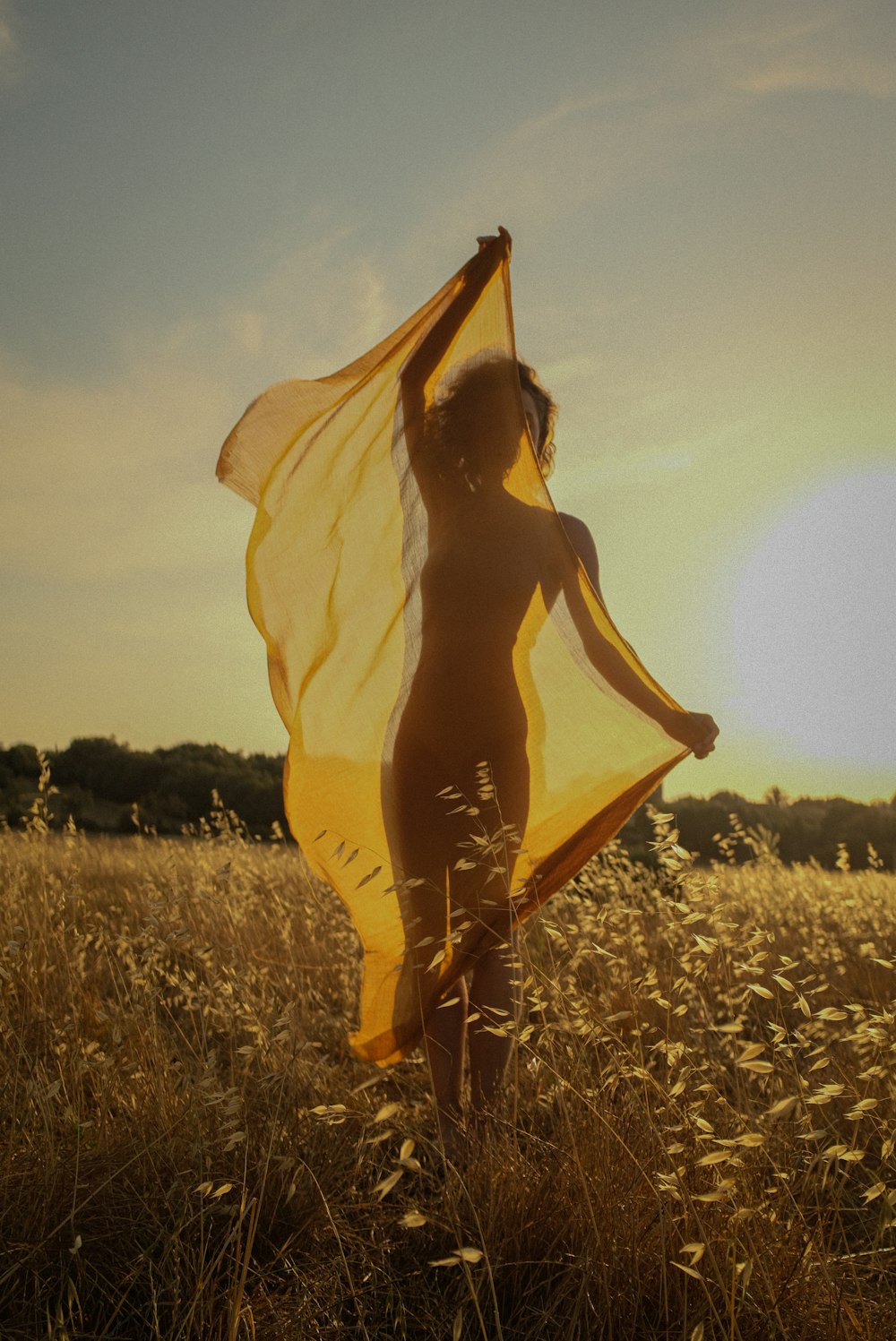 a woman standing in a field holding a yellow scarf