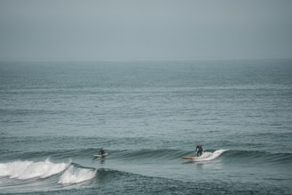 An instructor patiently helping a student balance on their surfboard in the gentle waves.