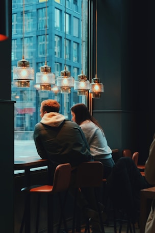 two people sitting at a table looking out a window