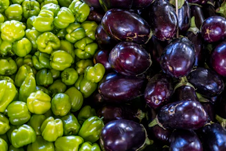 Exotic vegetables like purple eggplants and red bell peppers arranged on a rustic wooden table.