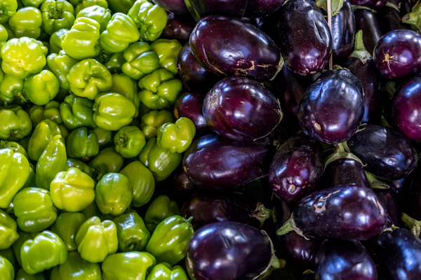 Exotic vegetables like purple eggplants and red bell peppers arranged on a rustic wooden table.