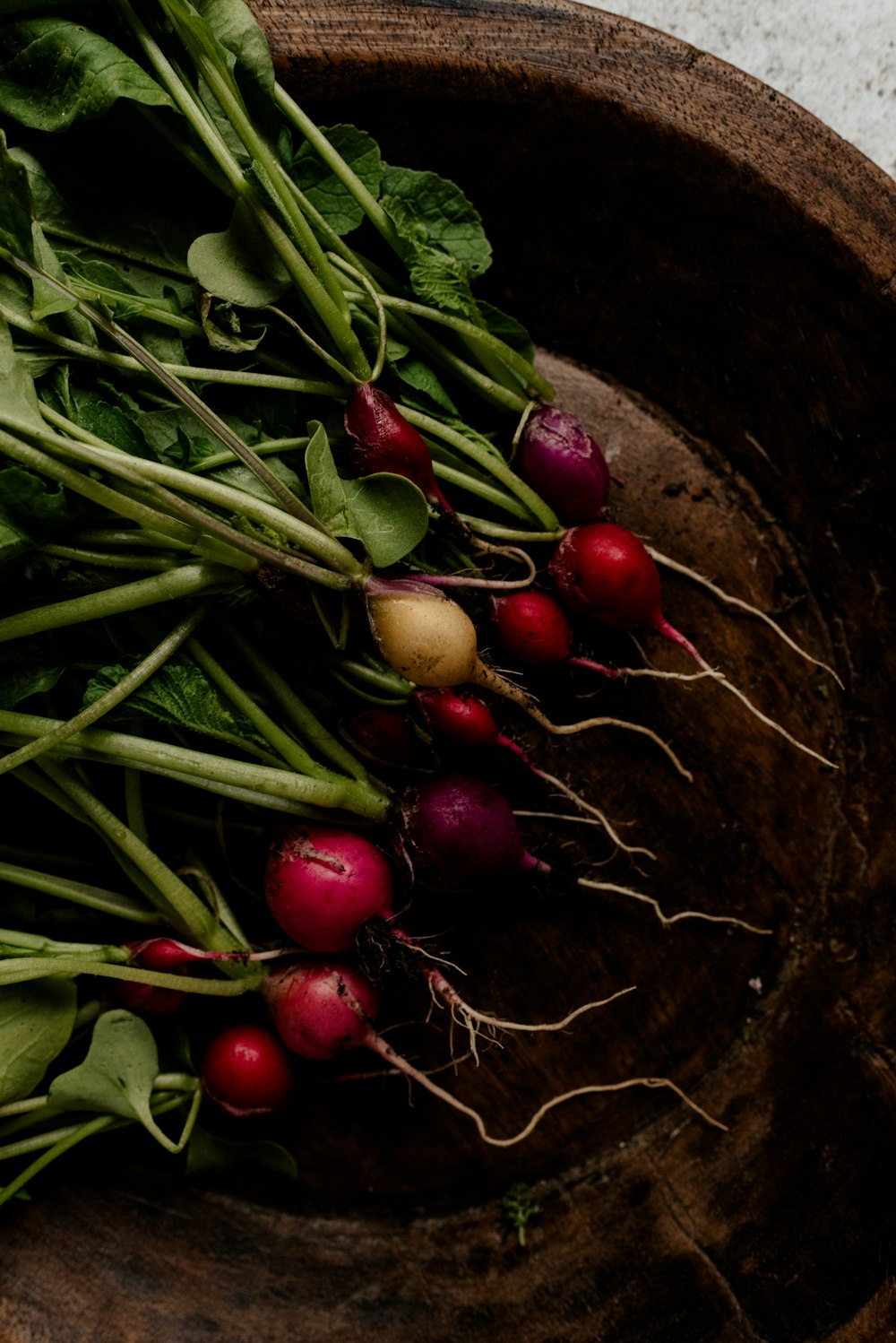 a wooden bowl filled with radishes and greens