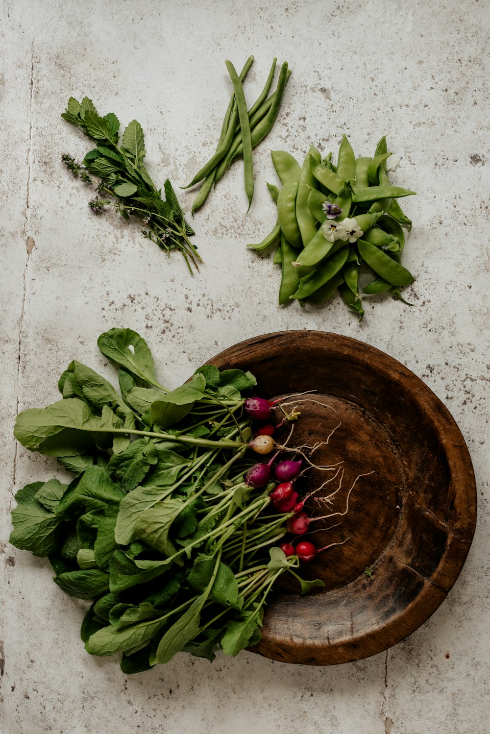 a wooden bowl filled with greens and radishes
