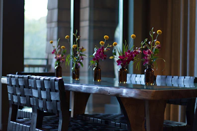 A vibrant dining area showcasing a solid wood table surrounded by colorful chairs, with fresh flowers adding a lively touch.