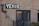 An exterior wall with a large sign that reads 'VENUE' in bold letters above a double-door entrance. An arrow points toward the venue, accompanied by a traditional outdoor wall lantern. A string of decorative lights is hanging above from left to right, adding a cozy and inviting ambiance. Small plants are visible at the bottom of the image, and a decorative metal gate partially obscures the entrance.