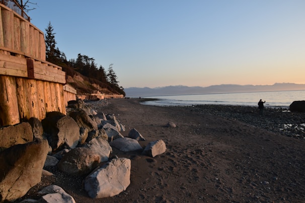 A coastal engineer taking water samples along a rocky shoreline at sunset.