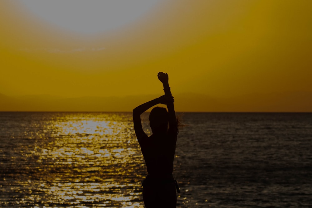 a woman standing on a beach with her arms in the air