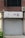 A storefront with a closed gray door and a sign above displaying Korean text. The sign includes a graphic of small colorful flowers and dots, and the surrounding building facade features brickwork. An air conditioning unit is mounted to the right of the sign.