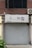 A storefront with a closed gray door and a sign above displaying Korean text. The sign includes a graphic of small colorful flowers and dots, and the surrounding building facade features brickwork. An air conditioning unit is mounted to the right of the sign.