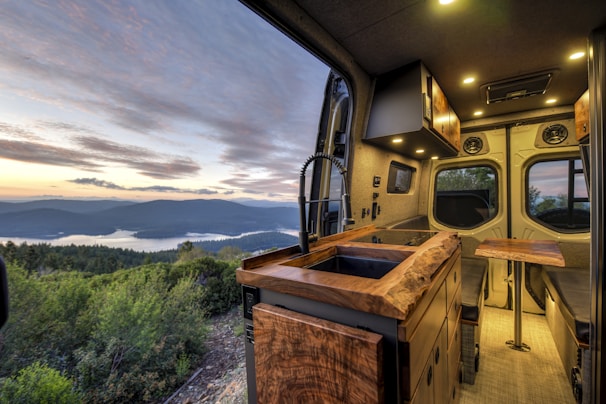 Finished van interior with soft lighting, a foldable bed, and panoramic windows revealing alpine scenery.