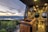 A cozy and modern camper van interior with wooden countertops and a sleek design. The view from the van's window overlooks a scenic landscape with a lake surrounded by hills and forests under a partly cloudy sky at sunset.