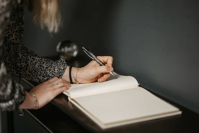 Close-up of a woman journaling with a rose gold pen on beige paper, surrounded by soft lighting.