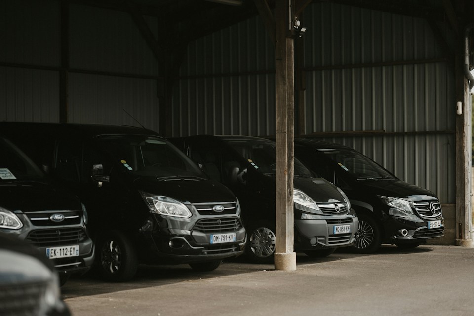 Black passenger vans parked under a covered lot awaiting fleet washing