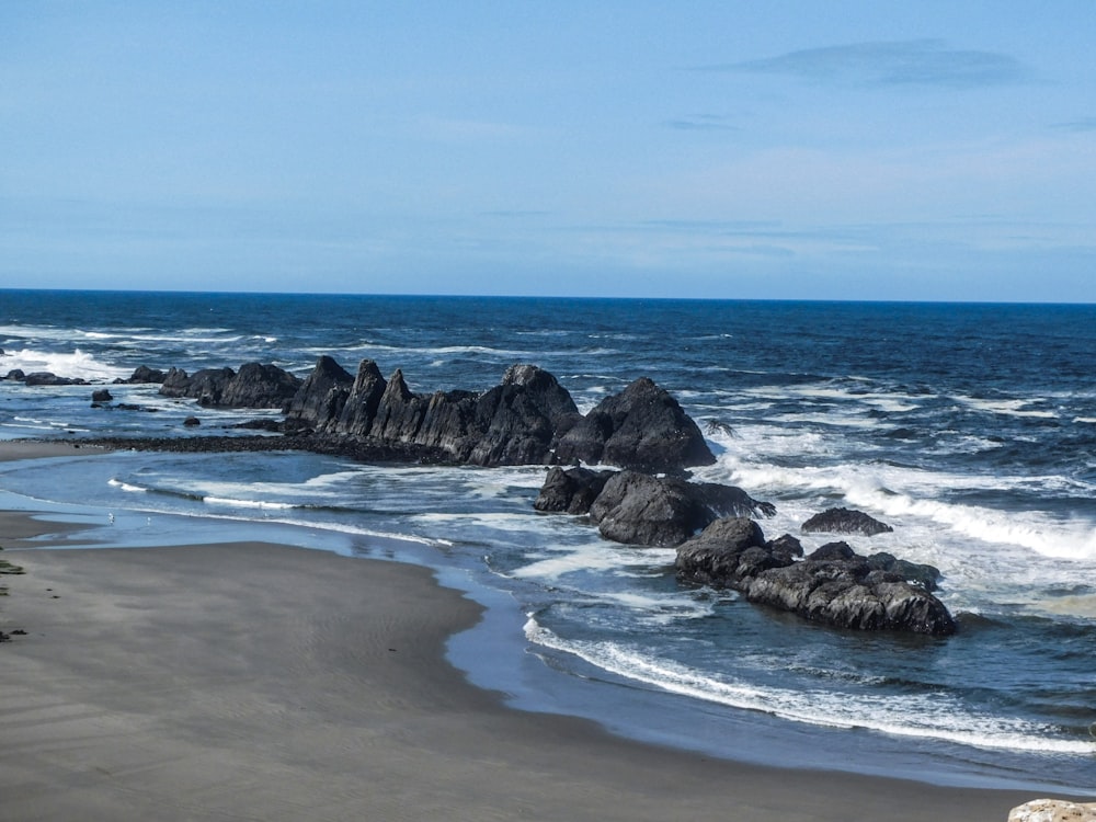 a sandy beach next to the ocean with rocks sticking out of the water