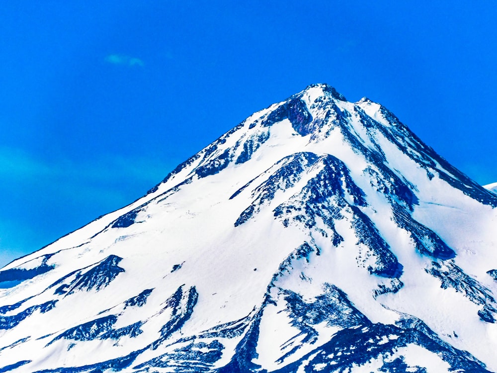 a very tall snow covered mountain under a blue sky