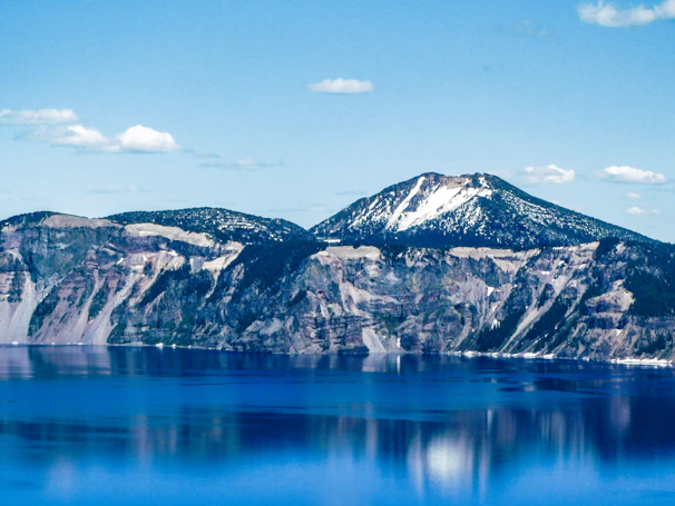 Clean horizon shot of a glacier-blue lake reflecting towering rocky cliffs dusted with snow.