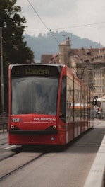 A red tram labeled 'Wabern' travels along a city street with historic architecture and faint hills visible in the background. The tram displays a message indicating it is CO2 neutral, emphasizing its environmental friendliness.