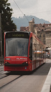 A red tram labeled 'Wabern' travels along a city street with historic architecture and faint hills visible in the background. The tram displays a message indicating it is CO2 neutral, emphasizing its environmental friendliness.