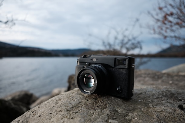 A close-up of a camera resting on a mossy rock beside a gentle stream in nature.