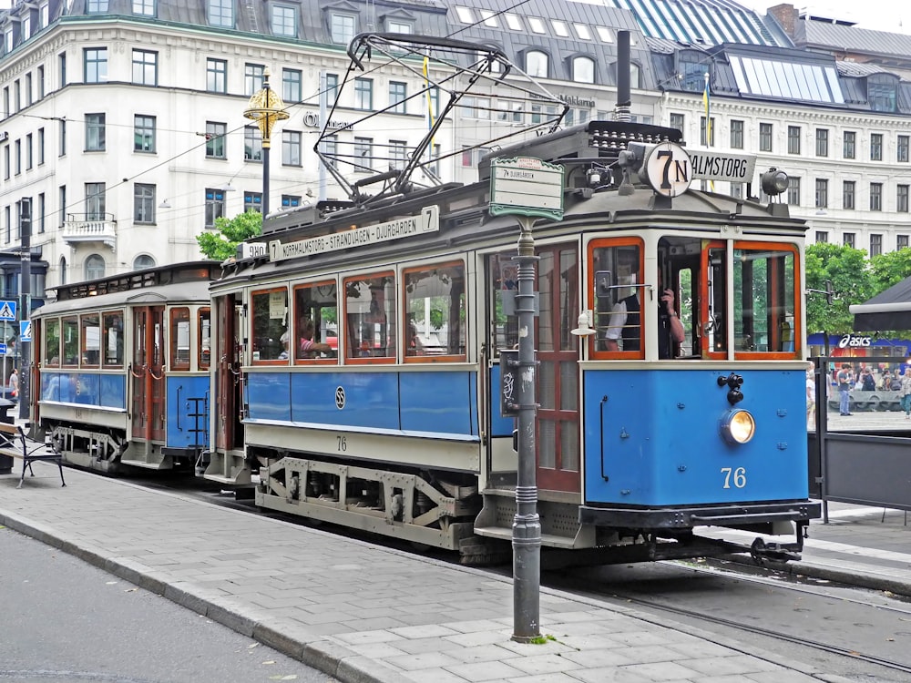 a blue trolley car traveling down a street next to tall buildings
