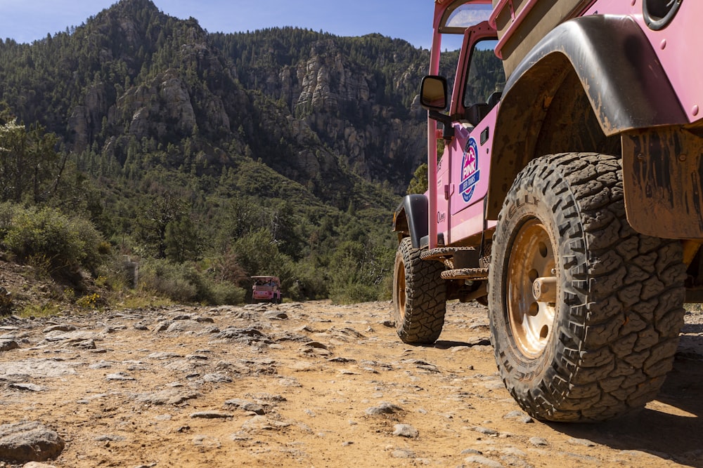a pink jeep driving down a dirt road