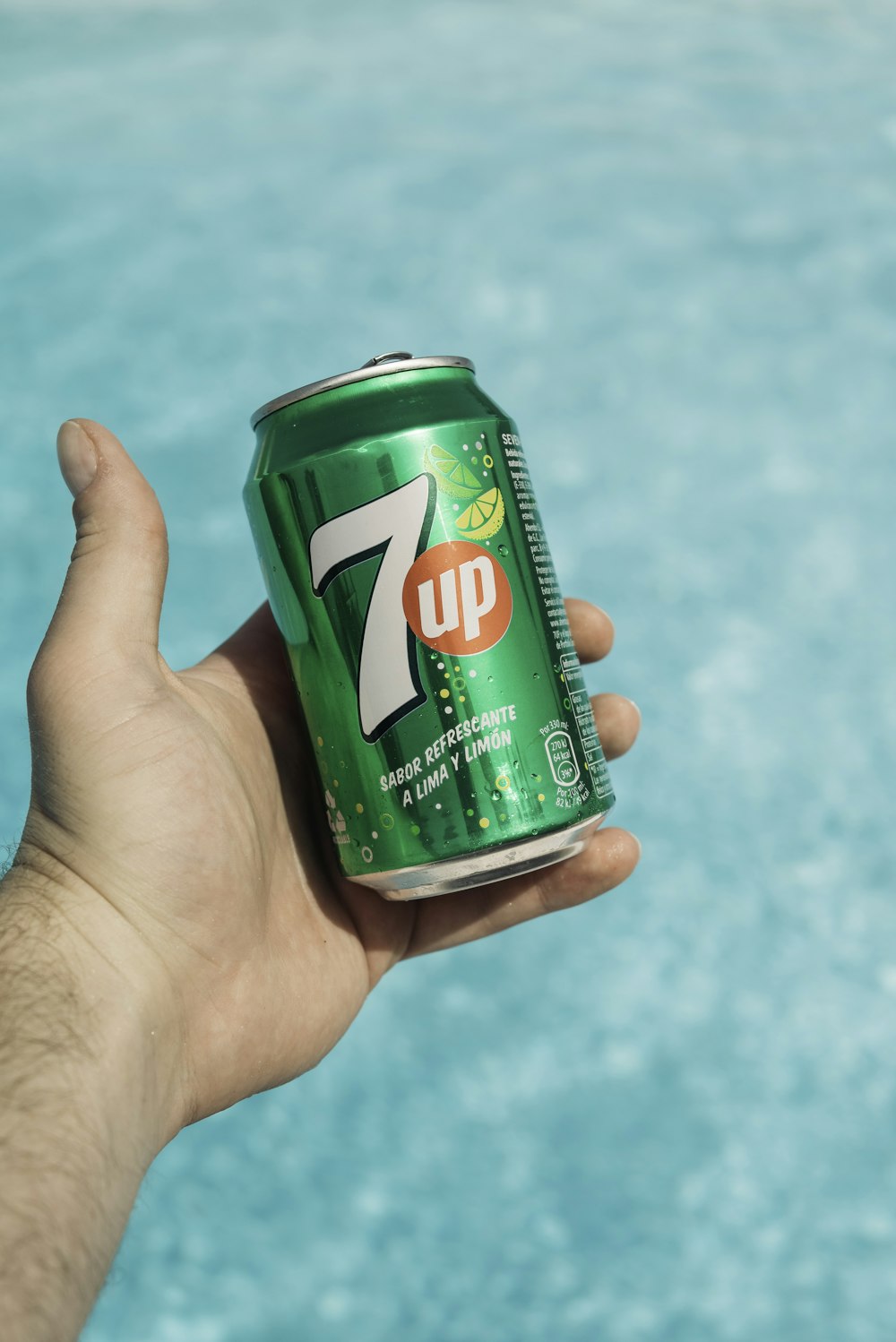 a hand holding a can of 7up by a pool