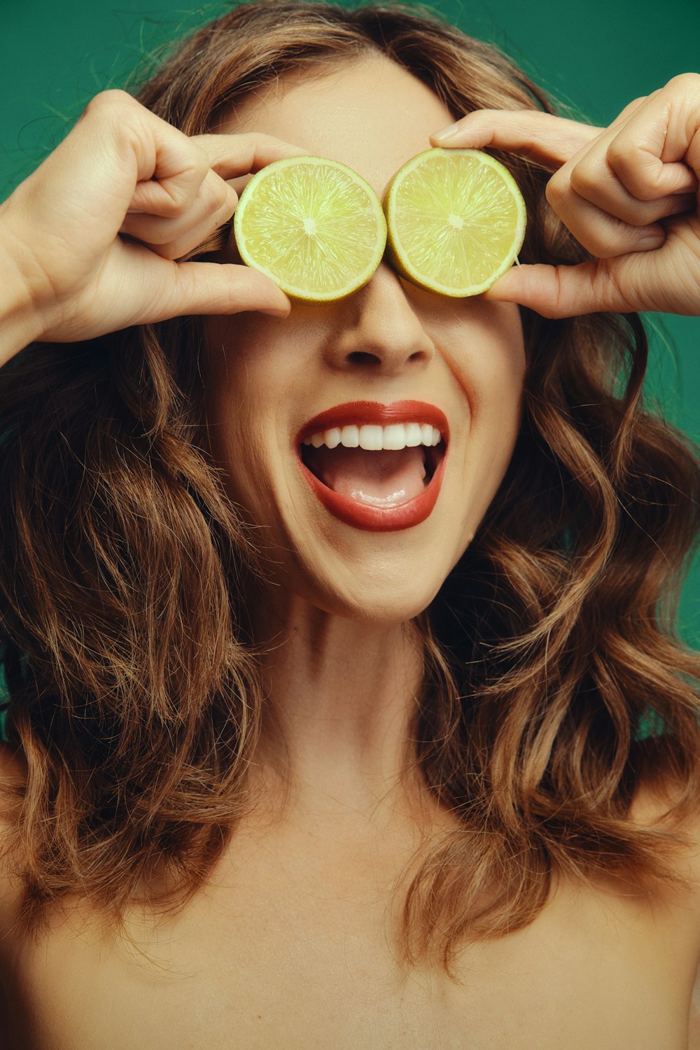 a woman holding two slices of limes over her eyes