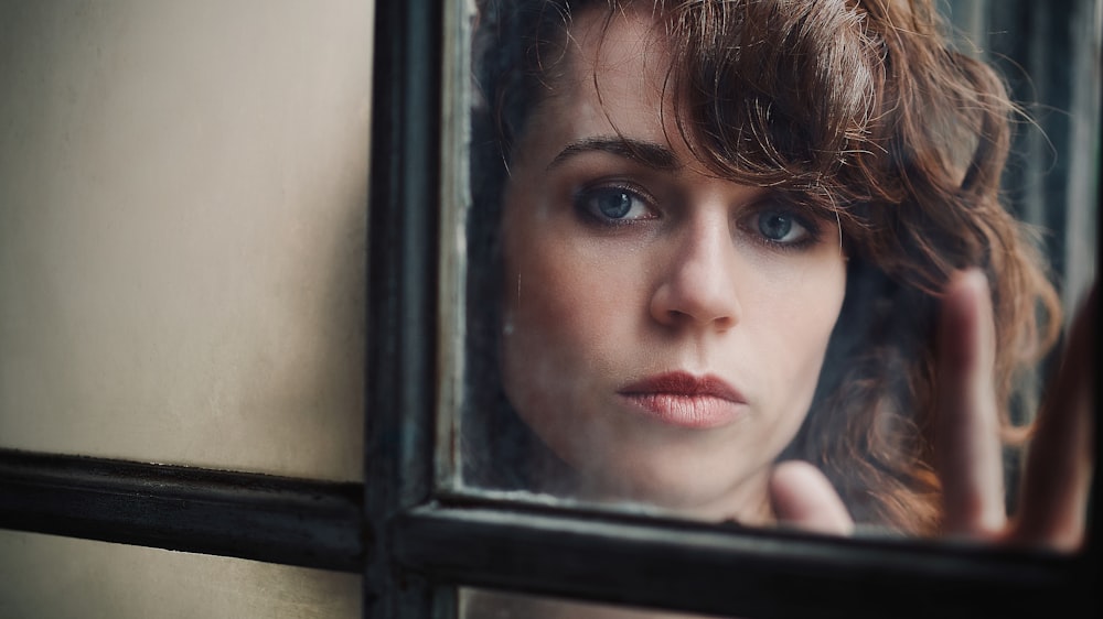 a woman looking out of a window with her hand on her head