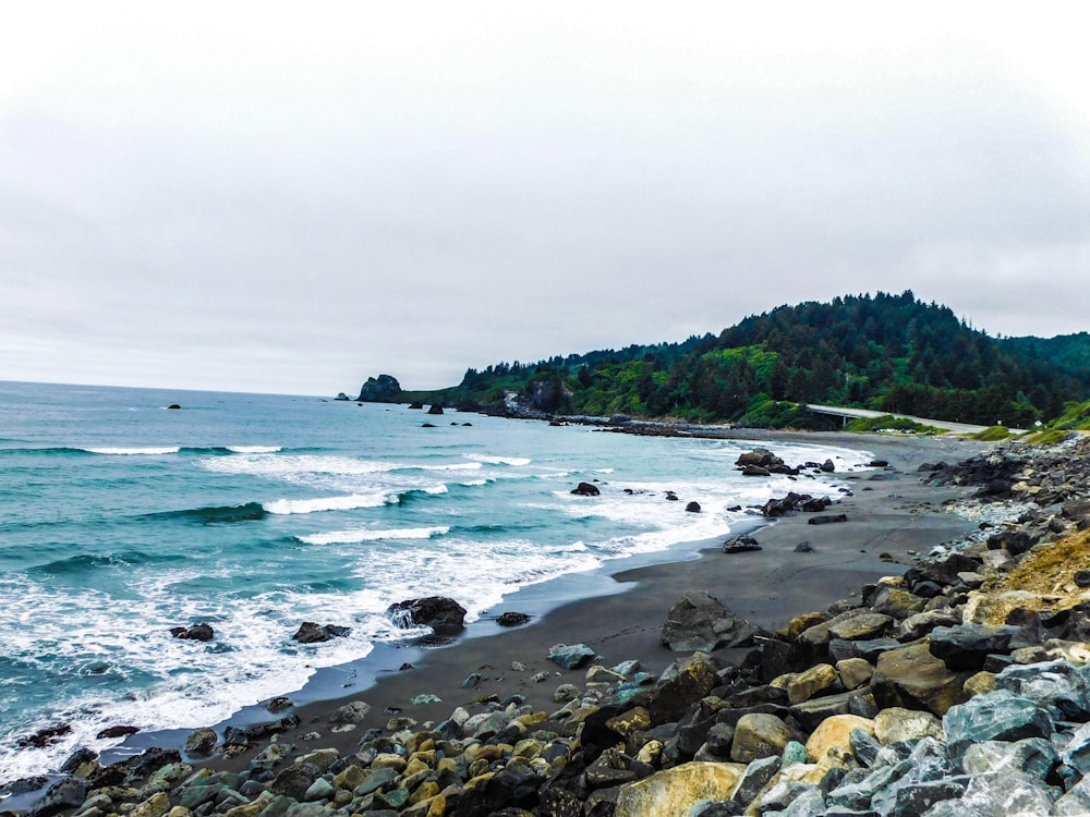 a rocky beach next to the ocean on a cloudy day