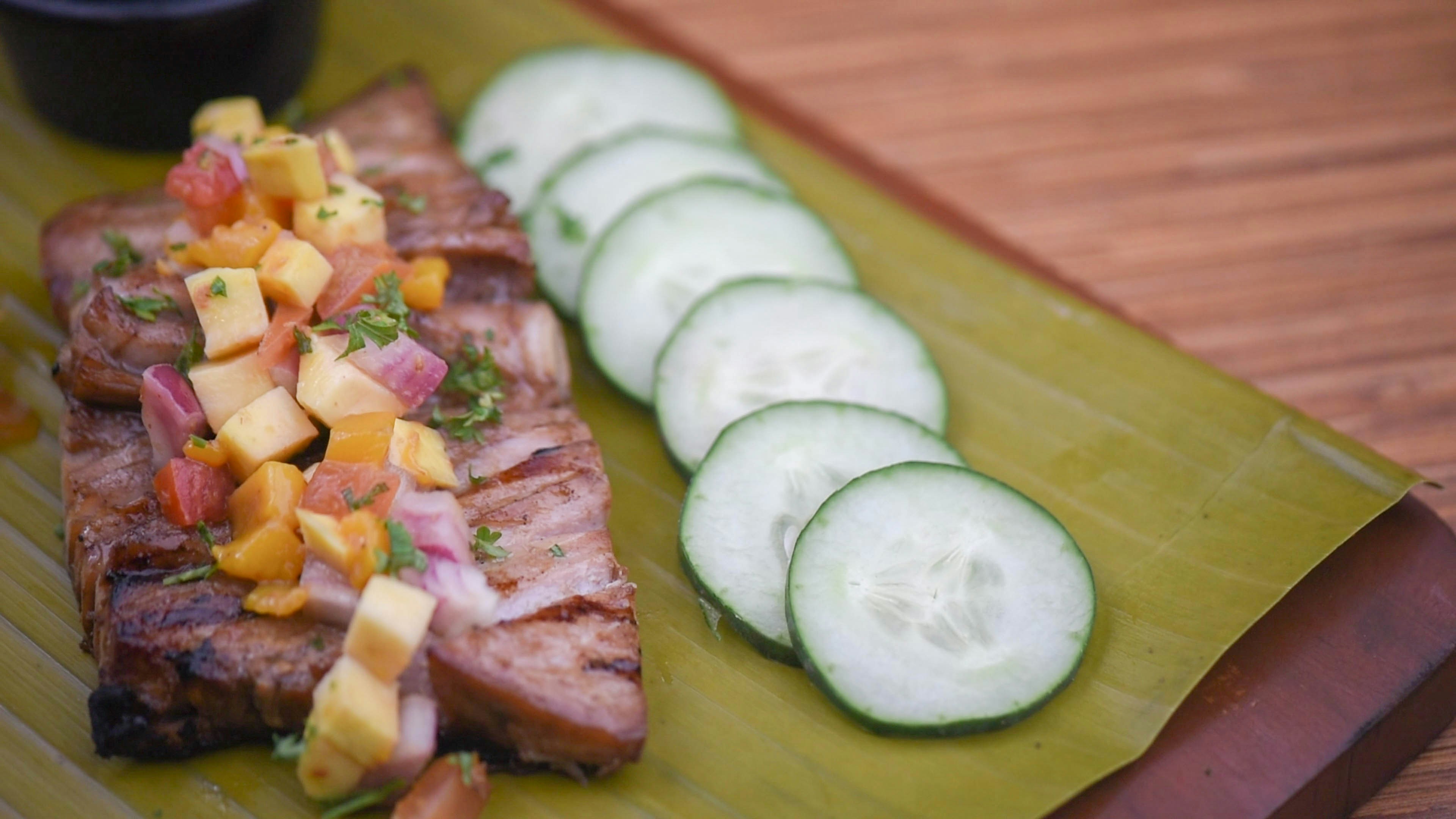 a green plate topped with a piece of meat and sliced cucumbers