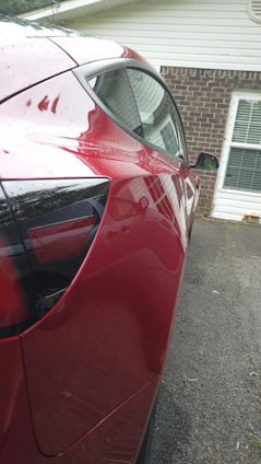 Close-up of a shiny red car parked in a sunlit driveway.