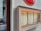 A glass display case attached to a textured wall showcases a menu. The menu is divided into sections, including 'Day Life' and 'Cocktails', listing items like coffee drinks, juices, and classic cocktails. The case is slightly tilted, and there is a reflection of passersby in the adjacent glass window, enhancing the urban vibe.