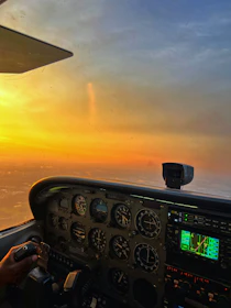 Close-up of a pilot’s hands adjusting cockpit controls, bathed in warm light from the setting sun.