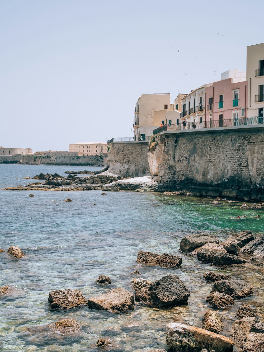 a body of water with rocks and buildings in the background