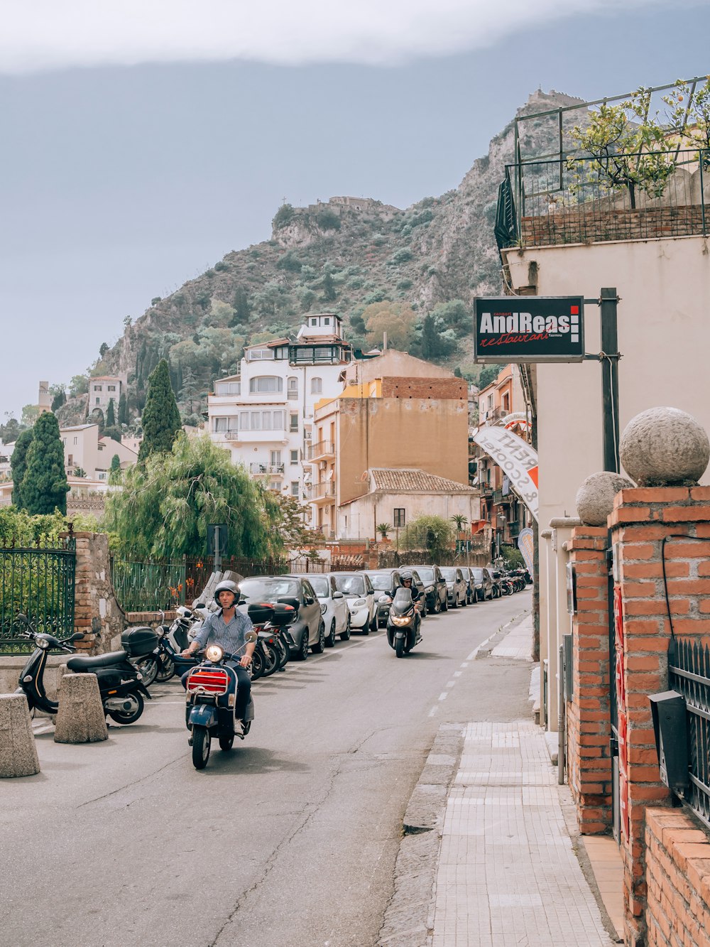 a man riding a motorcycle down a street next to parked cars