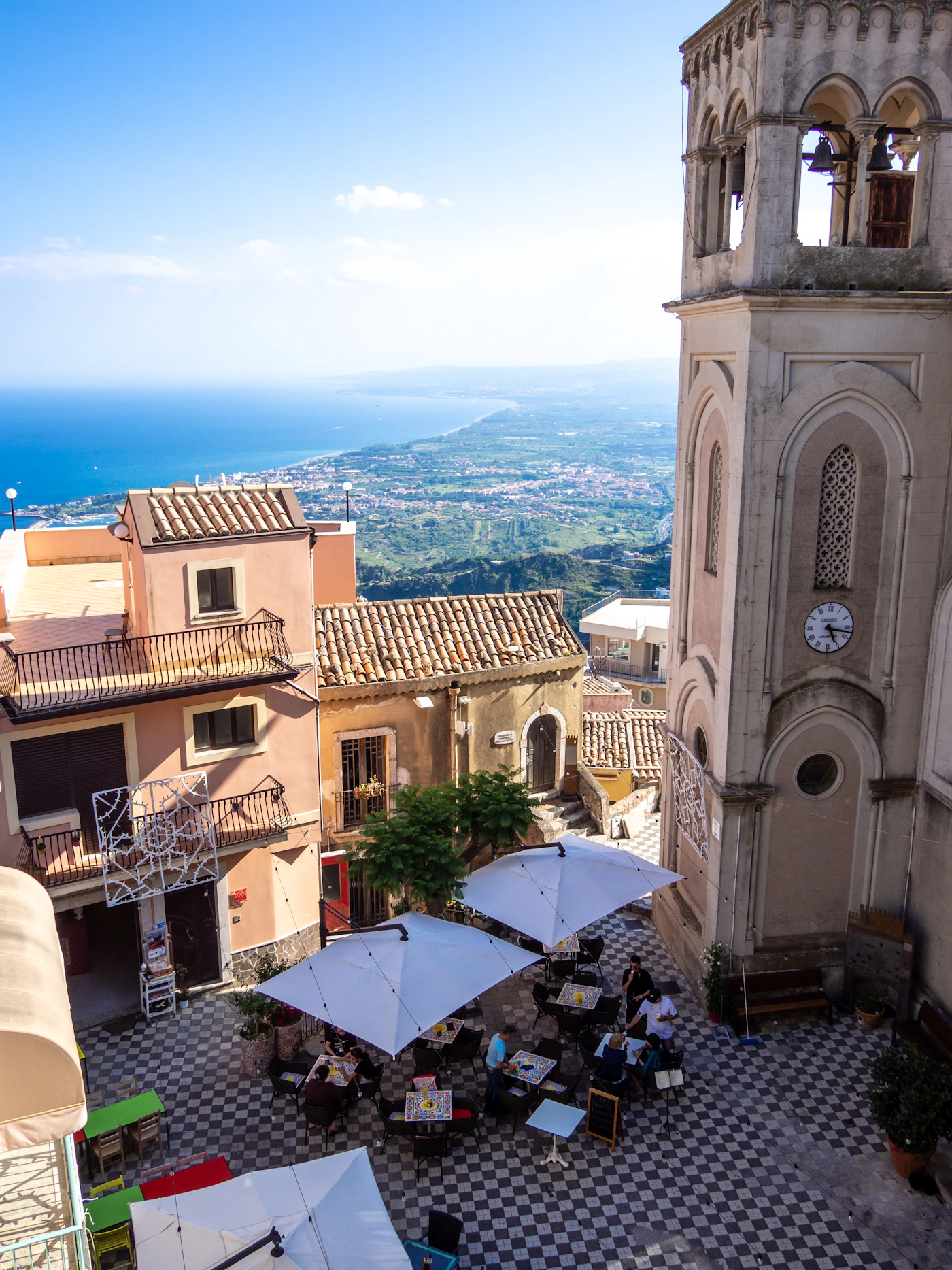 The ornate baroque clock tower of Taormina Sicily rising above the old town rooftops with warm golden stone and a clear blue Mediterranean sky with the town spread out below