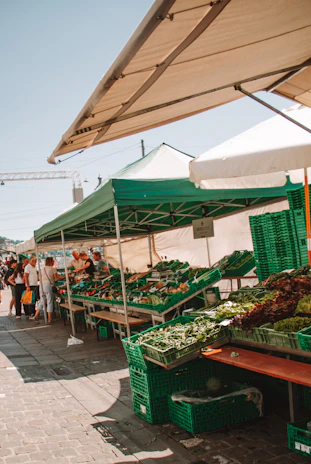 A lively farmers' market scene with families browsing fresh organic products and savoring homemade treats from Bibi Holy Foods.