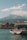 A serene waterfront scene with a boat named 'Saphir' moored in the foreground, flying a Swiss flag. The background features majestic mountains under a clear blue sky, accompanied by a few scattered clouds. Several buildings line the distant shore, also adorned with Swiss flags, creating a picturesque and calm setting.