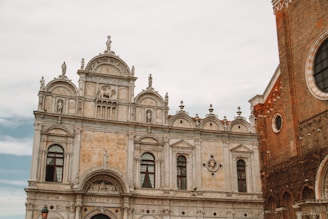 A historic building showcases intricate architectural details, including arches, columns, and statues adorning the façade. The structure exhibits a blend of stone and decorative sculptures, prominently featuring symmetrical design elements and classical motifs.