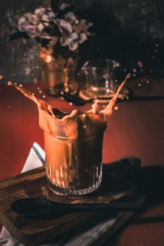 a glass filled with liquid sitting on top of a wooden cutting board