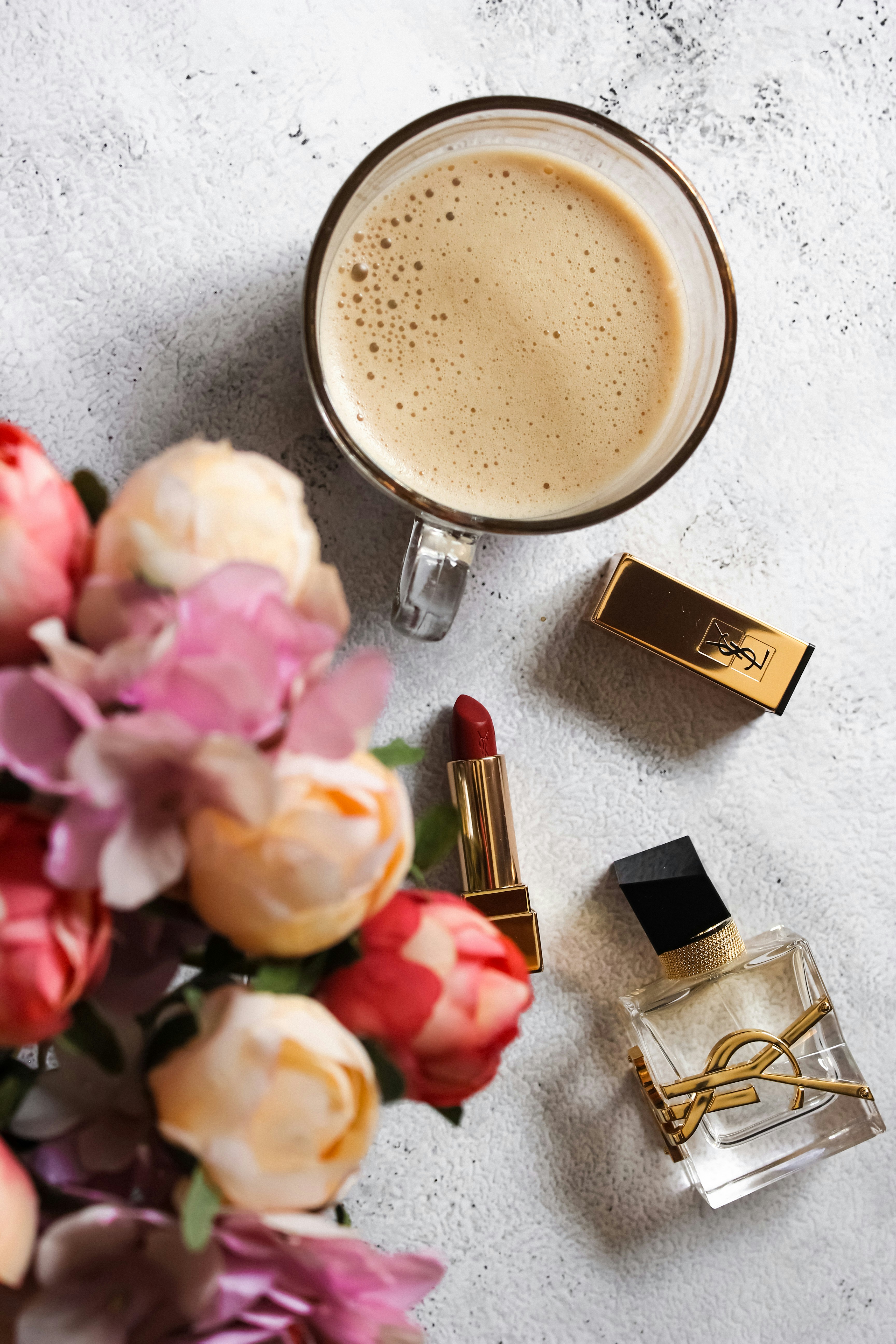 a cup of coffee next to lipstick and flowers