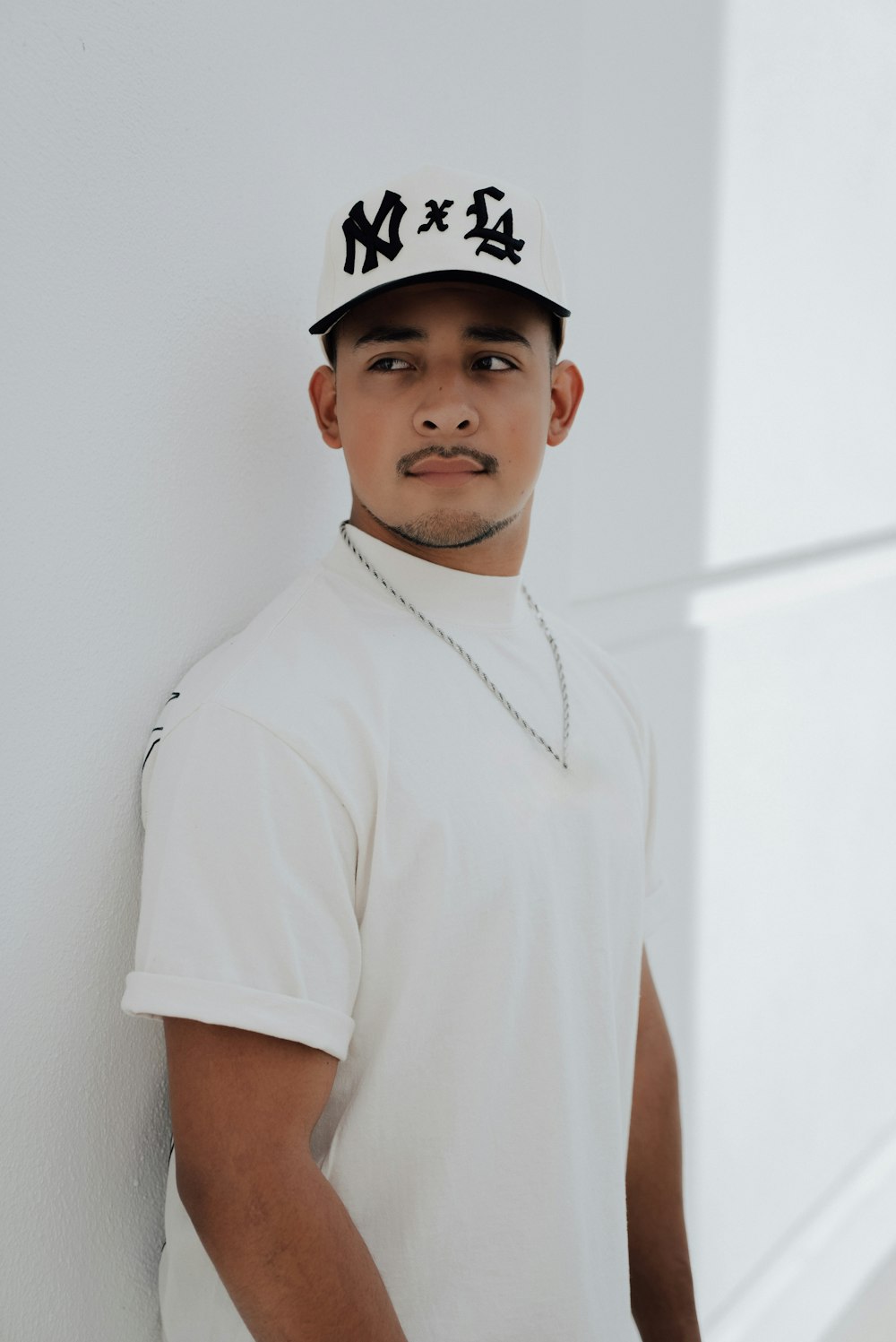 a young man wearing a baseball cap leaning against a wall